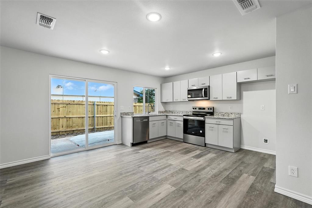 4613 Tarry Drive Garland, TX 75043 - Photo 8 of 38 a kitchen with stainless steel appliances granite countertop a stove top oven a sink dishwasher a refrigerator and white cabinets with wooden floor