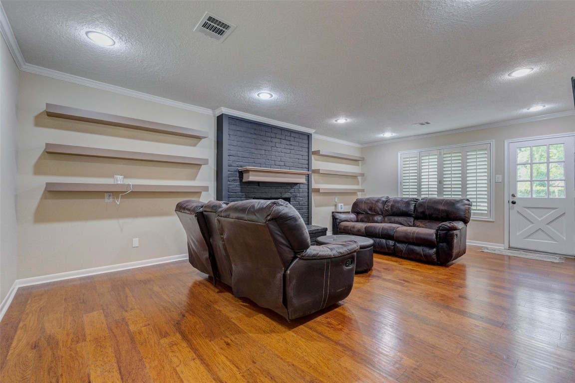 6710 Falling Waters Drive Spring, TX 77379 - Photo 12 of 45 This inviting living room features hardwood floors, a dark brick accent wall with built-in shelves, Recessed lighting, and a large window with wood shutters that provide ample light, while a glass-paneled door offers outdoor access.