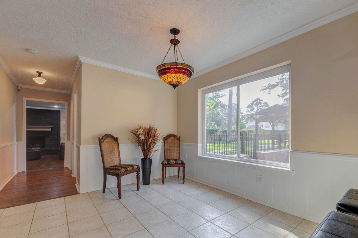 6710 Falling Waters Drive Spring, TX 77379 - Photo 18 of 45 The breakfast room features large windows overlooking the garden, neutral walls, and tile flooring. A decorative light fixture and wainscoting add character, while the adjacent hallway leads to a cozy living area with a fireplace.