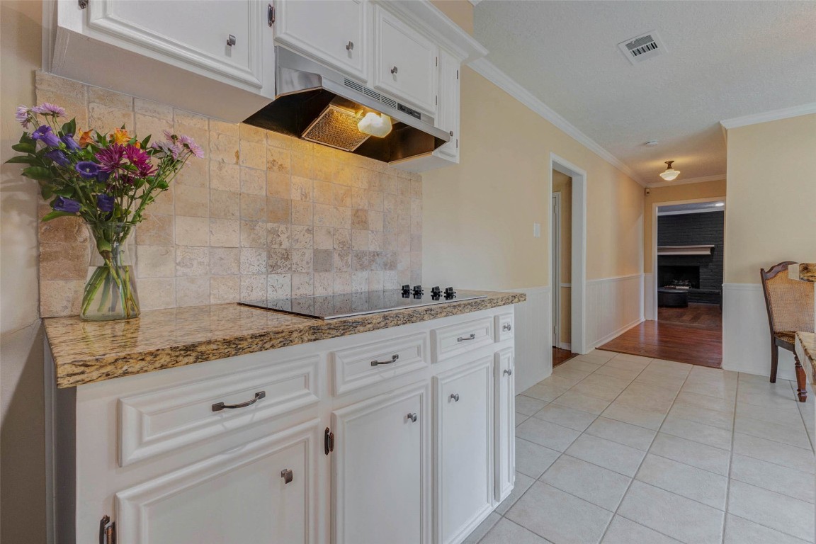 6710 Falling Waters Drive Spring, TX 77379 - Photo 19 of 45 This kitchen features white cabinetry, a granite countertop, and a tile backsplash, creating a clean and inviting space. An open hallway leads to a cozy living area with a visible fireplace, enhancing the home's warmth and charm.