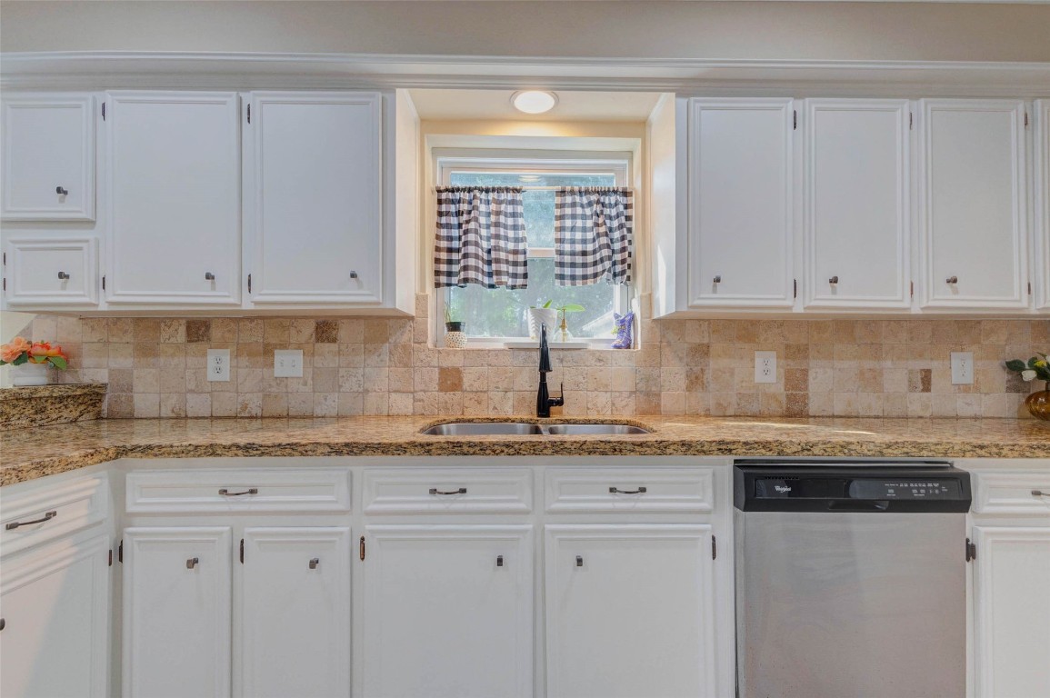 6710 Falling Waters Drive Spring, TX 77379 - Photo 20 of 45 The kitchen features solid-wood white cabinetry, granite countertops, a black faucet, and a stainless steel dishwasher. The backsplash is tiled in neutral tones, and a window above the sink provides natural light.