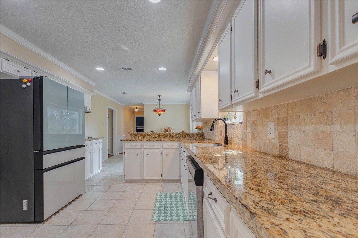 6710 Falling Waters Drive Spring, TX 77379 - Photo 21 of 45 This kitchen features granite countertops, white cabinets, a modern stainless steel refrigerator, and a tiled backsplash, creating a bright and spacious atmosphere.