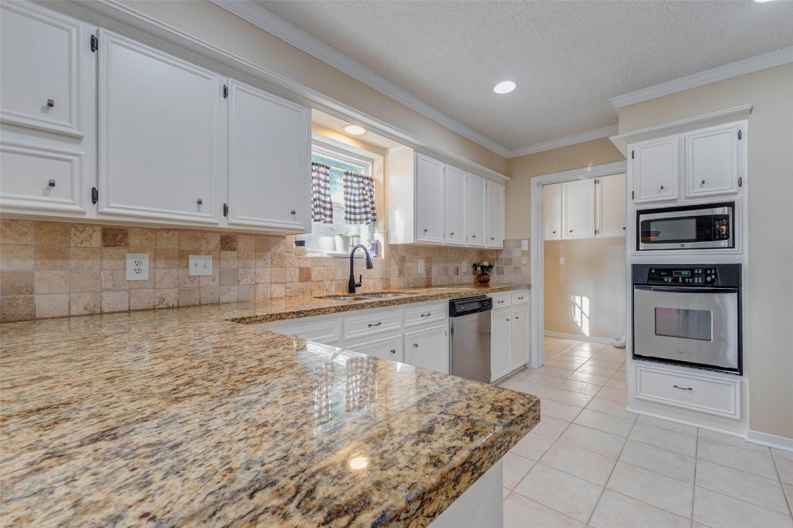 6710 Falling Waters Drive Spring, TX 77379 - Photo 22 of 45 Elegant granite countertops, white cabinetry, and modern stainless steel appliances. A light tile backsplash complements the bright, airy atmosphere, enhanced by natural light from a window above the sink.