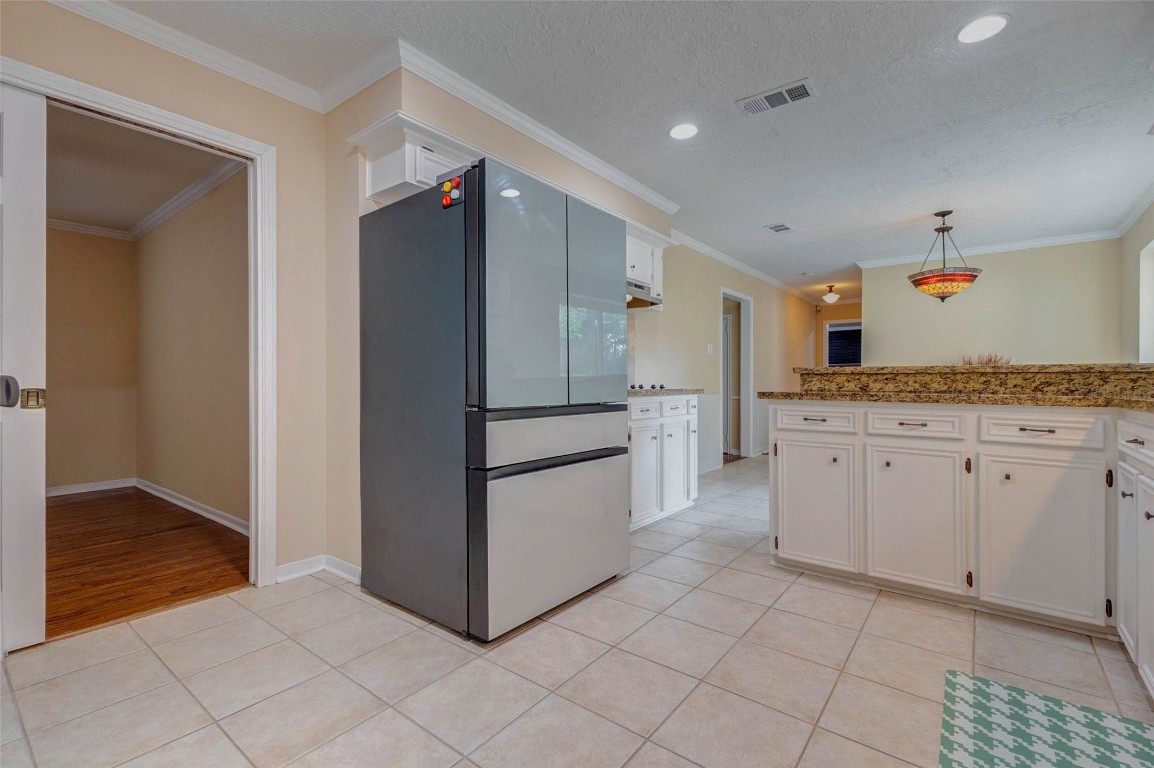 6710 Falling Waters Drive Spring, TX 77379 - Photo 23 of 45 Bright and spacious kitchen with modern appliances, ample white cabinetry, and granite countertops. Features tiled flooring, a stylish light fixture, and an adjacent open area with wood flooring.