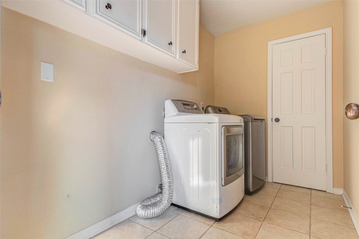 6710 Falling Waters Drive Spring, TX 77379 - Photo 24 of 45 This photo features a well-lit laundry room with tiled flooring, equipped with a washer and dryer. It includes upper cabinets for storage and has a neutral color palette, providing a clean and functional space.