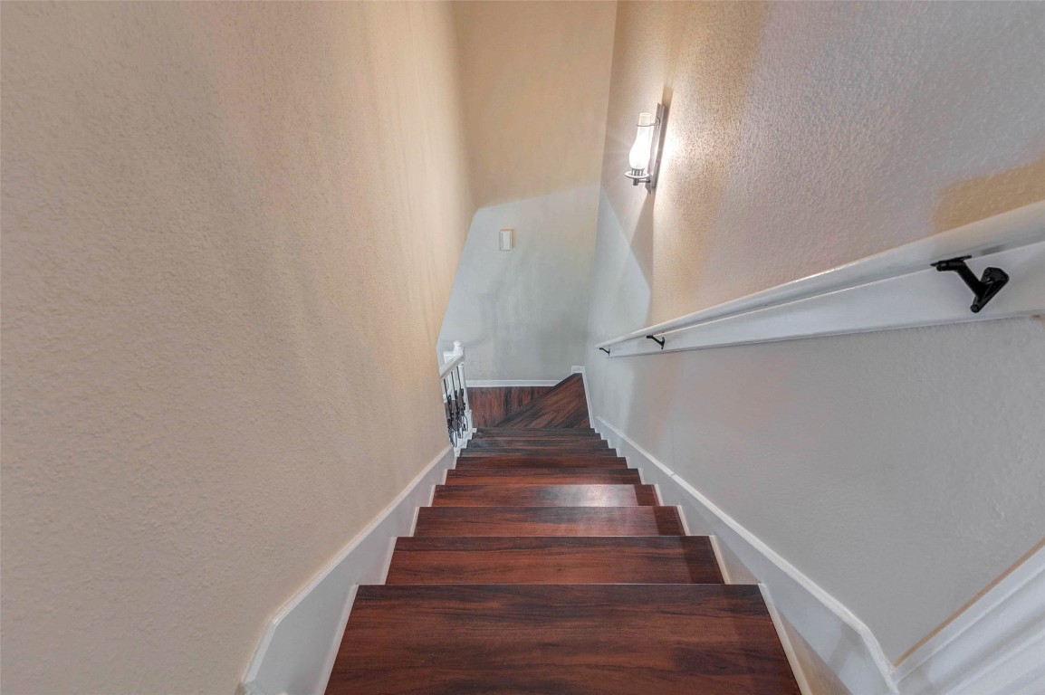 6710 Falling Waters Drive Spring, TX 77379 - Photo 27 of 45 This photo shows a well-lit staircase with wooden steps and white railings, leading down to a lower floor. The walls are painted in a neutral tone, providing a warm and inviting atmosphere.