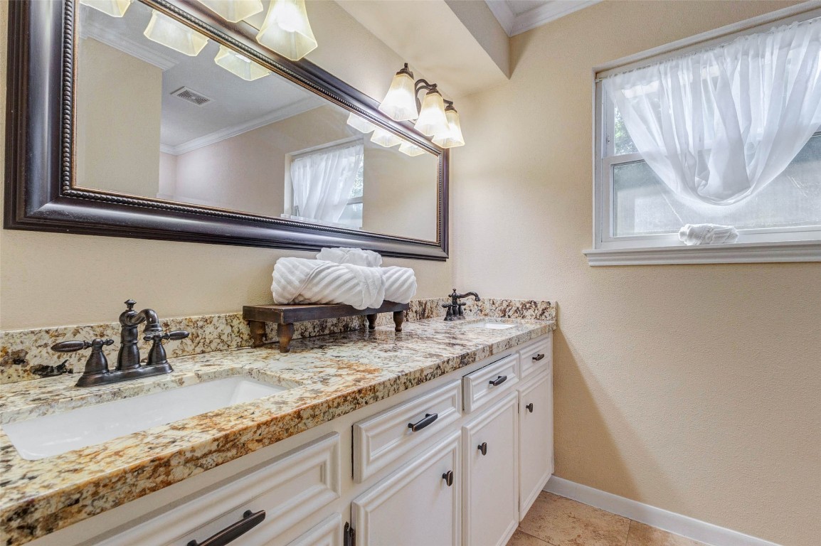 6710 Falling Waters Drive Spring, TX 77379 - Photo 37 of 45 The primary suite bathroom features a dual-sink vanity with granite countertops, elegant fixtures, and a large framed mirror. Soft lighting and a window with sheer curtains enhance the bright, inviting atmosphere.