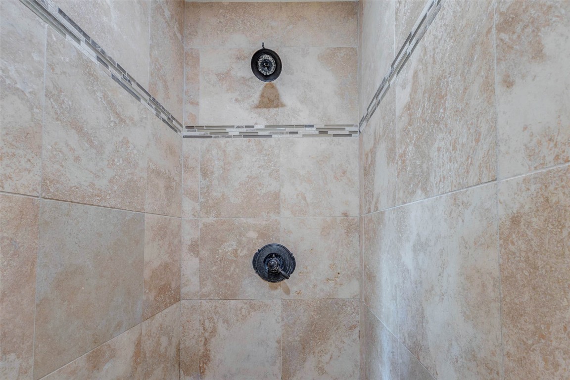 6710 Falling Waters Drive Spring, TX 77379 - Photo 39 of 45 This photo showcases a shower with elegant beige tile walls and decorative accent strips, featuring a sleek, dark shower fixture for a modern and stylish bathroom look.
