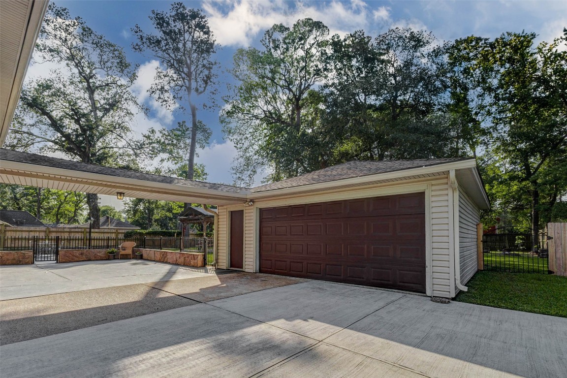 6710 Falling Waters Drive Spring, TX 77379 - Photo 40 of 45 This photo features a spacious driveway leading to a double garage with a covered walkway. Surrounded by tall trees, the area offers a blend of privacy and natural beauty.