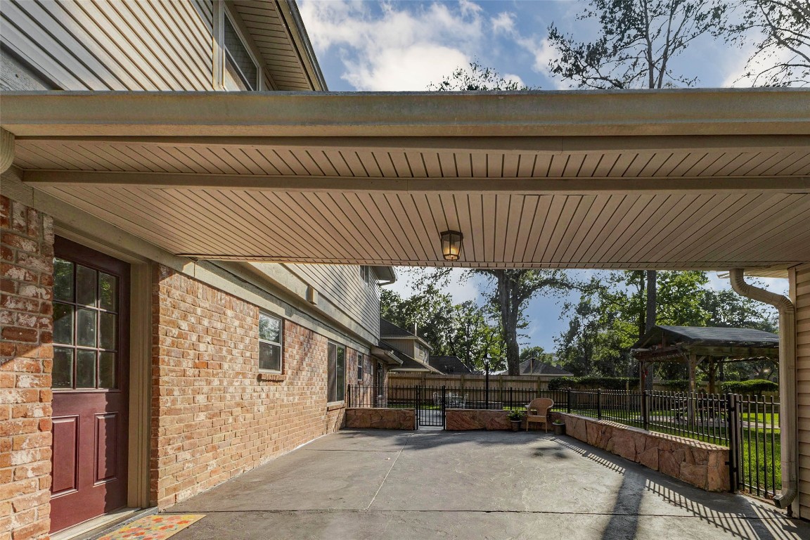 6710 Falling Waters Drive Spring, TX 77379 - Photo 42 of 45 This photo showcases a covered driveway with a brick exterior, leading to a fenced backyard. It features a well-maintained patio area with seating, surrounded by mature trees for added privacy and shade.