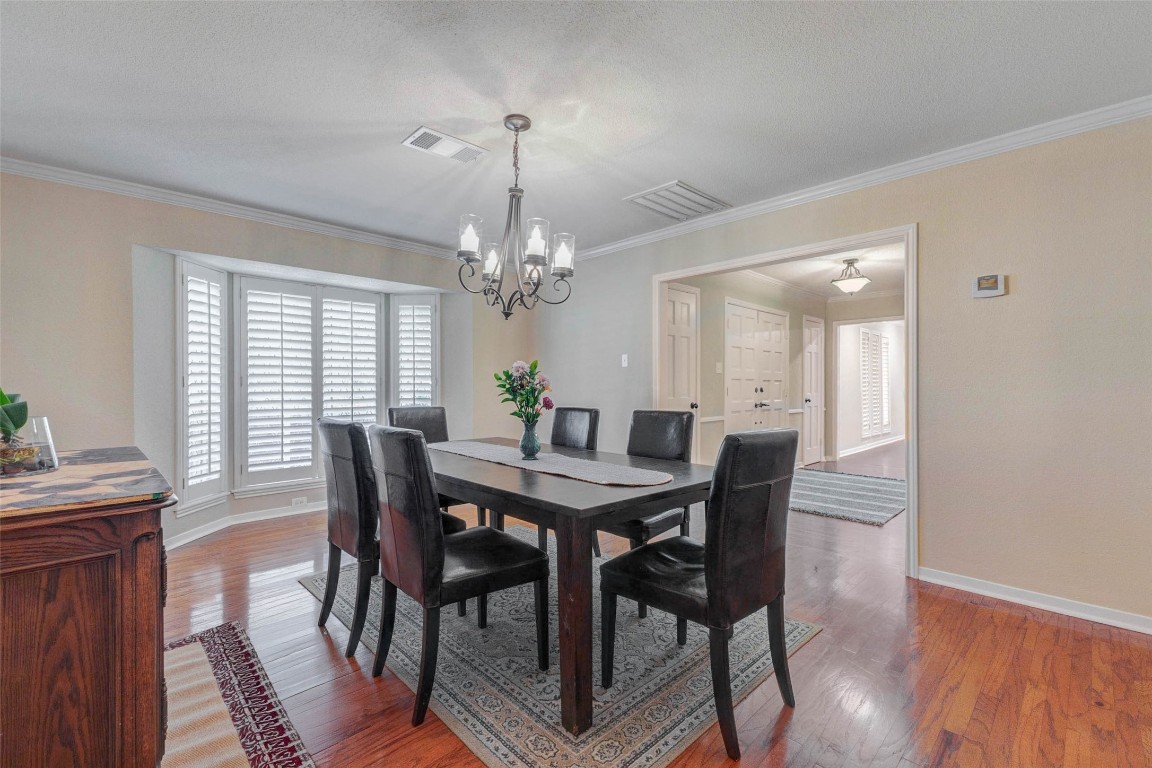 6710 Falling Waters Drive Spring, TX 77379 - Photo 9 of 45 The dining room has warm hardwood floors and a central chandelier. Windows with wood shutters that offer natural light. The space is open and inviting, leading into a hallway with additional lighting.