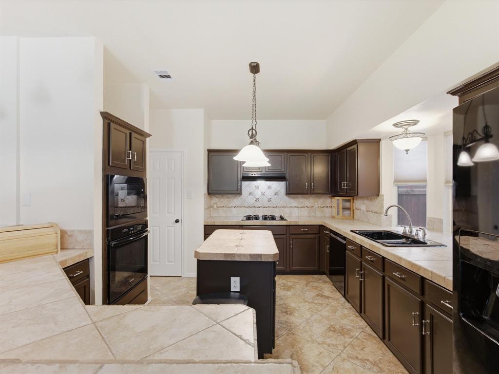 4008 Falcon Ridge Drive Haltom City, TX 76137 - Photo 10 of 40 Spacious kitchen featuring dark wood cabinetry, tile countertops, a center island with a breakfast bar, stainless steel double oven, and integrated built-in appliances