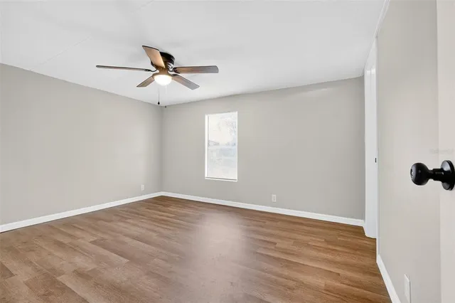 an empty room with wooden floor ceiling fan and windows