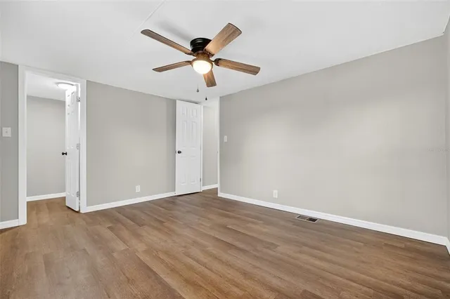 an empty room with wooden floor fan and windows