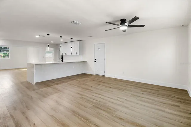 an empty room with wooden floor chandelier fan and windows