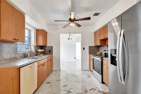 a kitchen with stainless steel appliances granite countertop a refrigerator a sink a stove and white cabinets with wooden floor