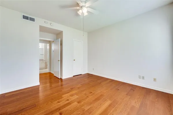 a view of an empty room with wooden floor and a ceiling fan
