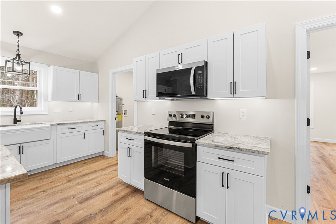 5132 Sunnyside Road Tappahannock, VA 22560 - Photo 11 of 28 a kitchen with stainless steel appliances white cabinets a sink a stove a microwave and wooden floors