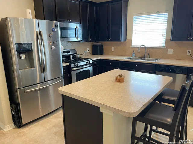 a kitchen with stainless steel appliances a refrigerator a sink a stove a table and chairs