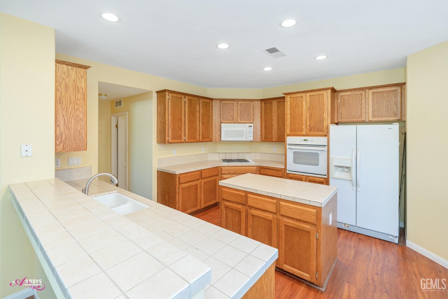 Undisclosed Address Bakersfield, CA 93312 - Photo 13 of 53 Kitchen with tiled counter, island, wood like floors extended into kitchen