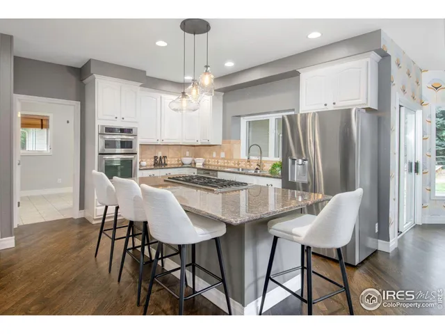 a kitchen with stainless steel appliances kitchen island granite countertop a dining table chairs and a refrigerator