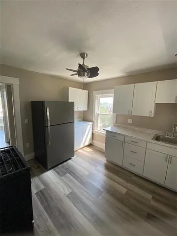 a kitchen with granite countertop a refrigerator oven a sink dishwasher and white cabinets with wooden floor