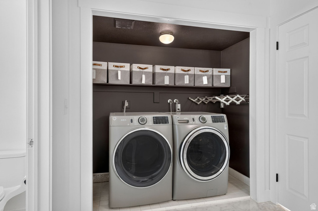 1979 Cave Hollow Way Bountiful, UT 84010 - Photo 23 of 59 Dedicated laundry area featuring a front-loading washer and dryer, wall-mounted shelving, overhead lighting, and a retractable drying rack