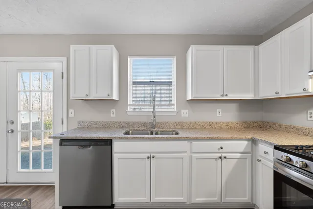 a kitchen with stainless steel appliances granite countertop white cabinets sink and window