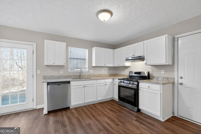 a kitchen with granite countertop stainless steel appliances a sink cabinets and wooden floor