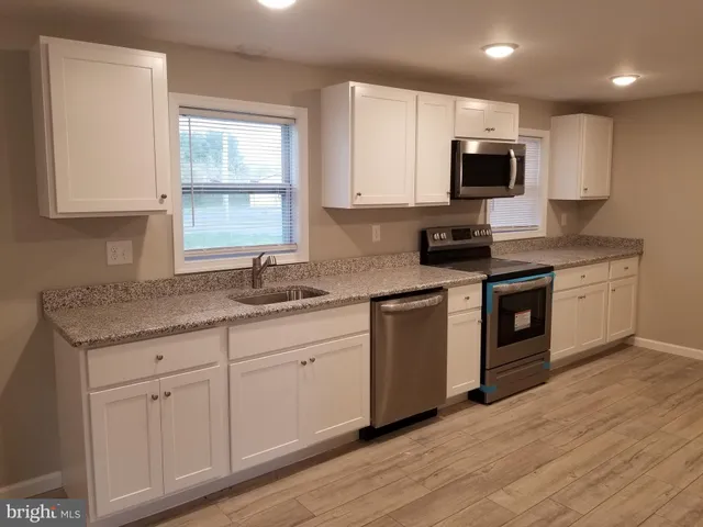 a kitchen with granite countertop a sink stainless steel appliances and white cabinets