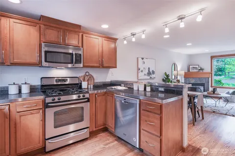 a kitchen with stainless steel appliances granite countertop wooden cabinets a sink a stove a refrigerator and island with wooden floors