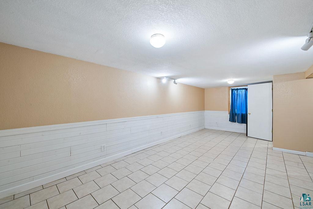 122 3rd Street Cloquet, MN 55720 - Photo 22 of 42 Spacious room featuring light-colored tile flooring, white wainscoting, and neutral-toned walls