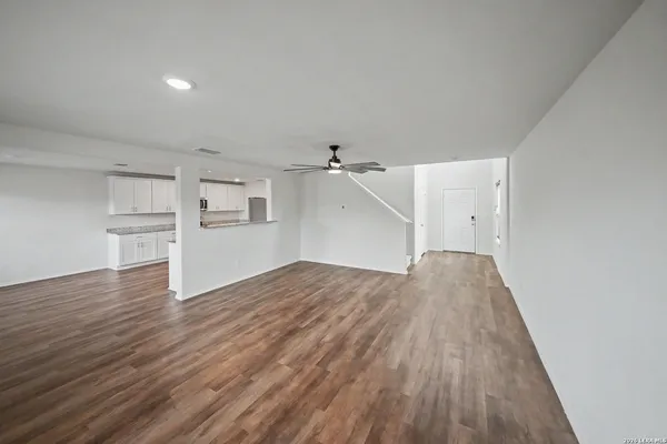 an empty room with wooden floor and kitchen view