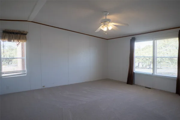 an empty room with a chandelier fan and windows