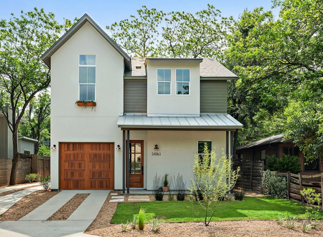 View of front facade with fence, a garage, concrete driveway, stucco siding, and a standing seam roof