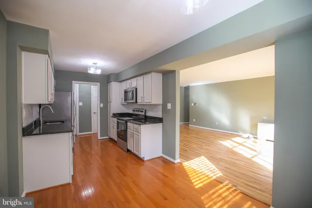 a view of a kitchen with kitchen island granite countertop a refrigerator cabinets and wooden floor