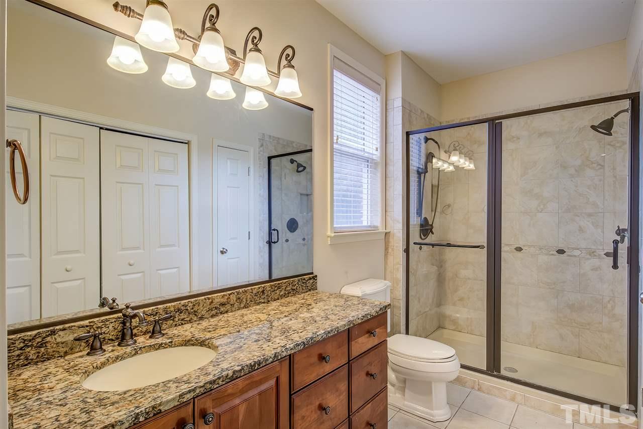 201 West Savannah Ridge Road, Unit 201 Holly Springs, NC 27540 - Photo 24 of 30 a bathroom with a granite countertop sink toilet a mirror a shower and vanity