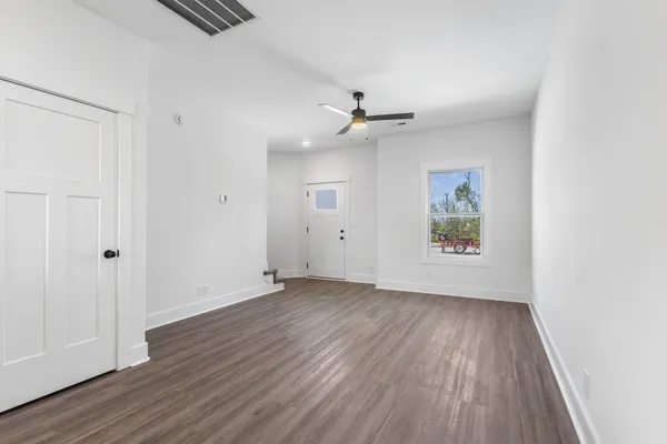 an empty room with wooden floor chandelier fan and windows
