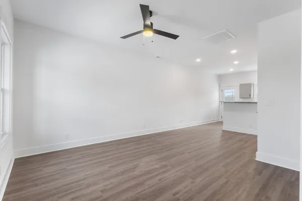 a view of an empty room with wooden floor and a ceiling fan