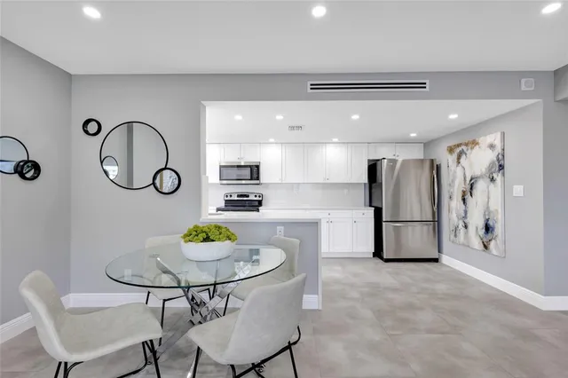 a kitchen with stainless steel appliances kitchen island granite countertop a refrigerator a stove a sink a dining table and chairs with wooden floor