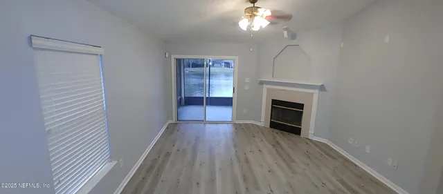 a view of an empty room with wooden floor fireplace and a window
