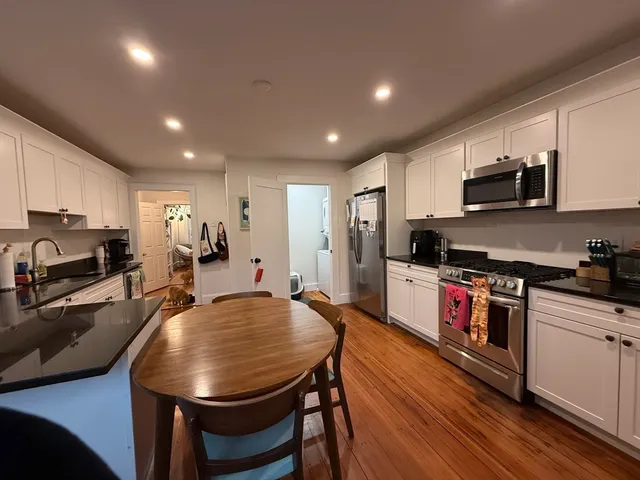 a kitchen with stainless steel appliances granite countertop a sink a stove a refrigerator cabinets and a dining table