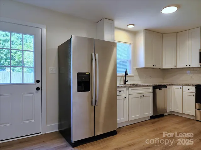 a kitchen with stainless steel appliances granite countertop a refrigerator a sink and white cabinets with wooden floor