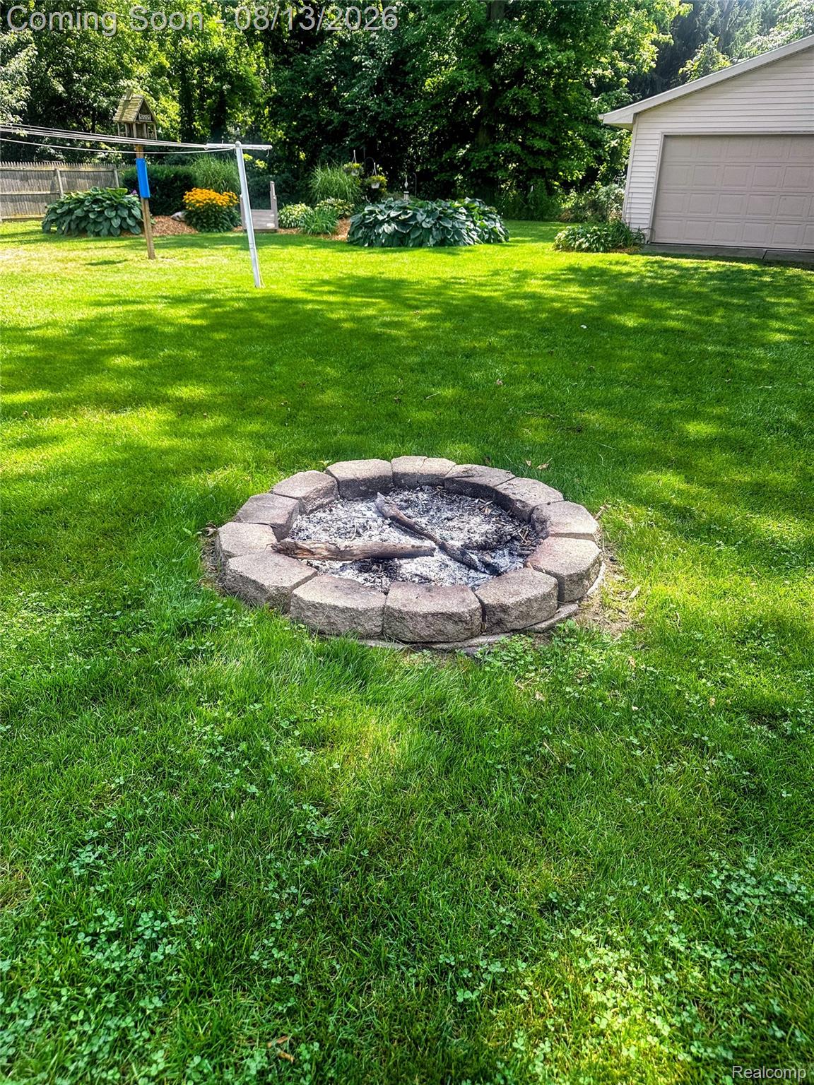 10361 Coldwater Road Flushing, MI 48433 - Photo 30 of 37 Expansive backyard featuring a stone-ringed fire pit, manicured lawn, established landscaping, and detached garage