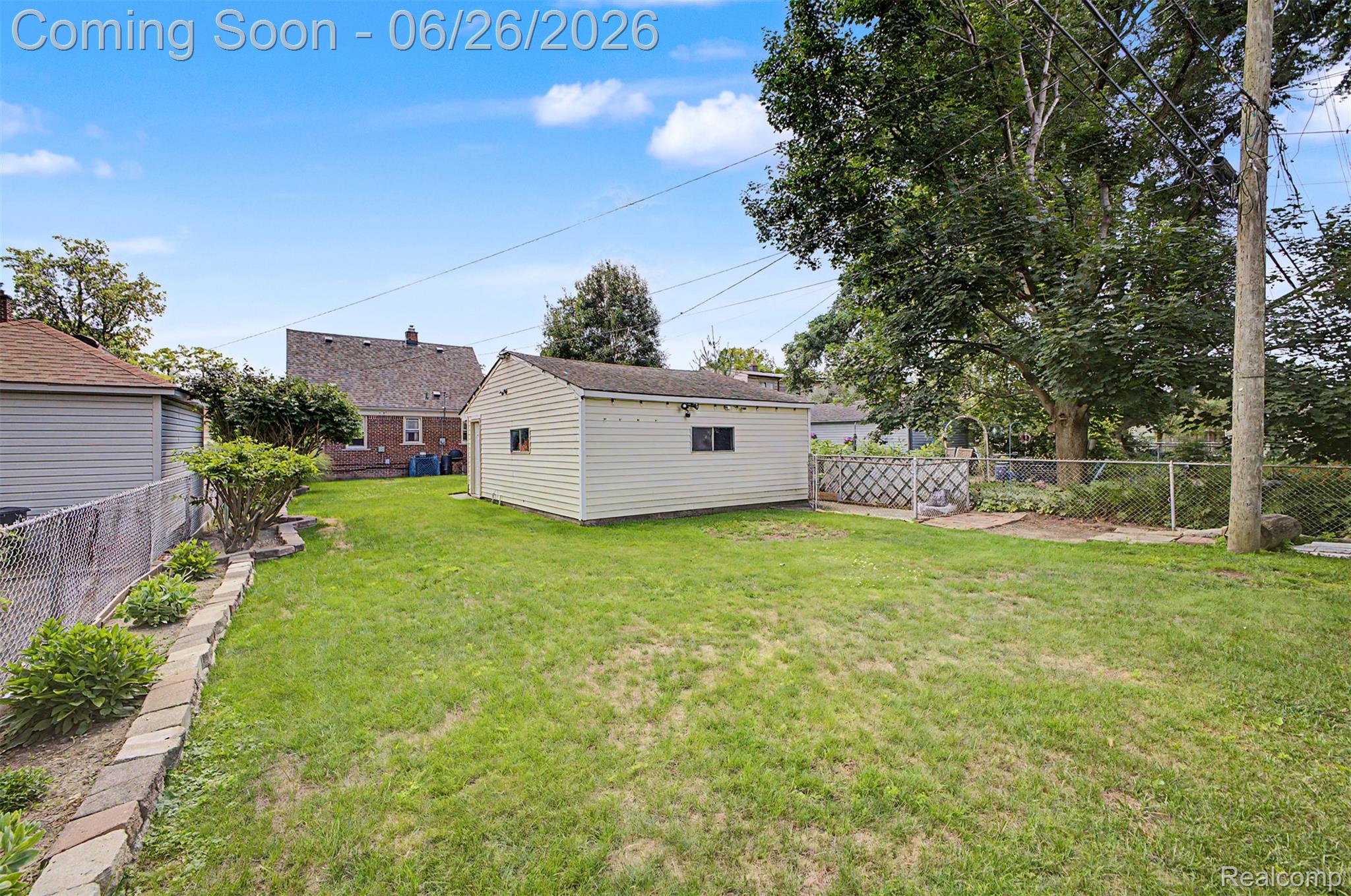 2216 Banner Street Dearborn, MI 48124 - Photo 33 of 34 Spacious backyard featuring a detached garage with vinyl siding, established garden bed with stone retaining wall, mature trees, and chain-link fencing