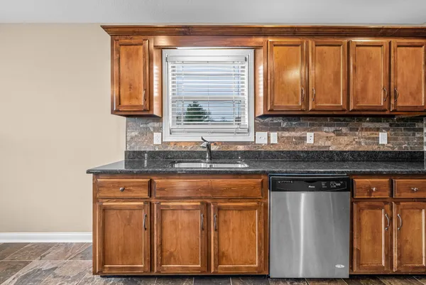 a kitchen with granite countertop wooden cabinets a sink and dishwasher next to a window