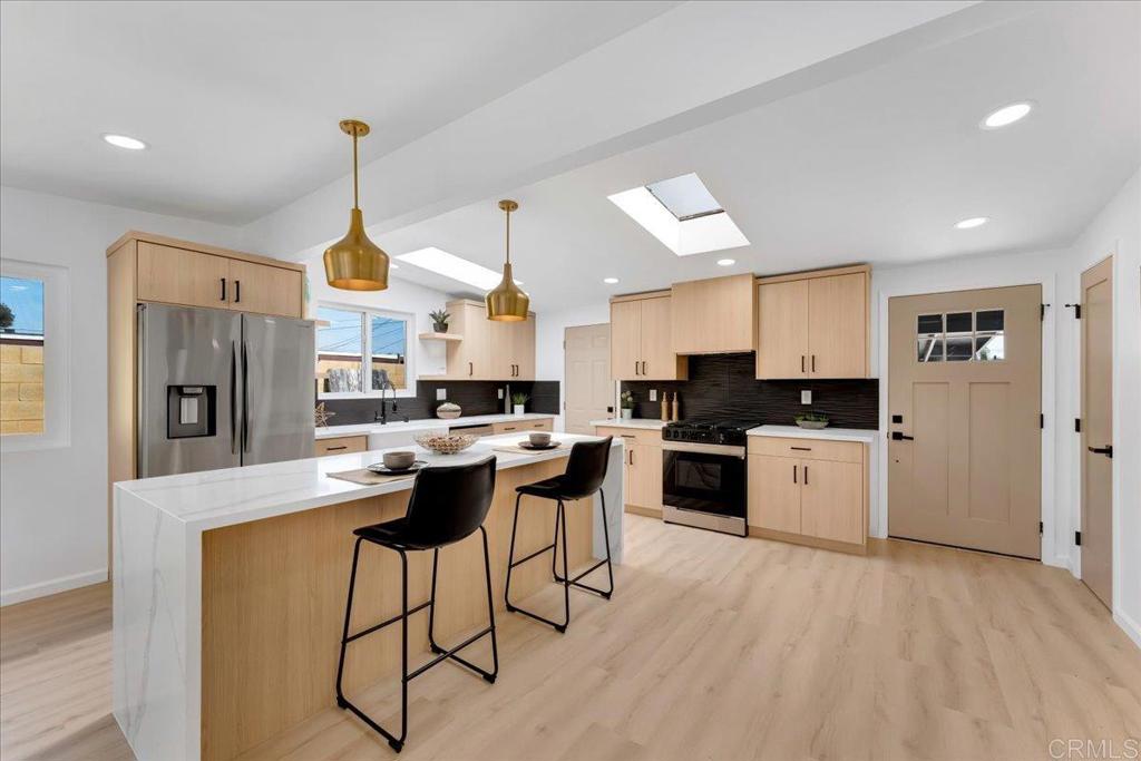a kitchen with stainless steel appliances kitchen island granite countertop a refrigerator a sink dishwasher a stove and white cabinets with wooden floor