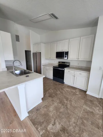 a kitchen with granite countertop a refrigerator a stove top oven and white cabinets