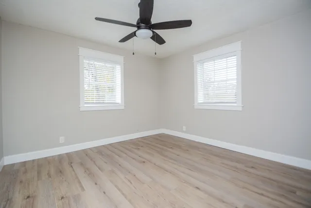 an empty room with wooden floor ceiling fan and windows