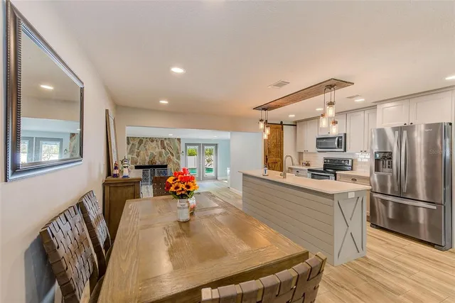 a kitchen with stainless steel appliances granite countertop a refrigerator a sink dishwasher a dining table and chairs with wooden floor